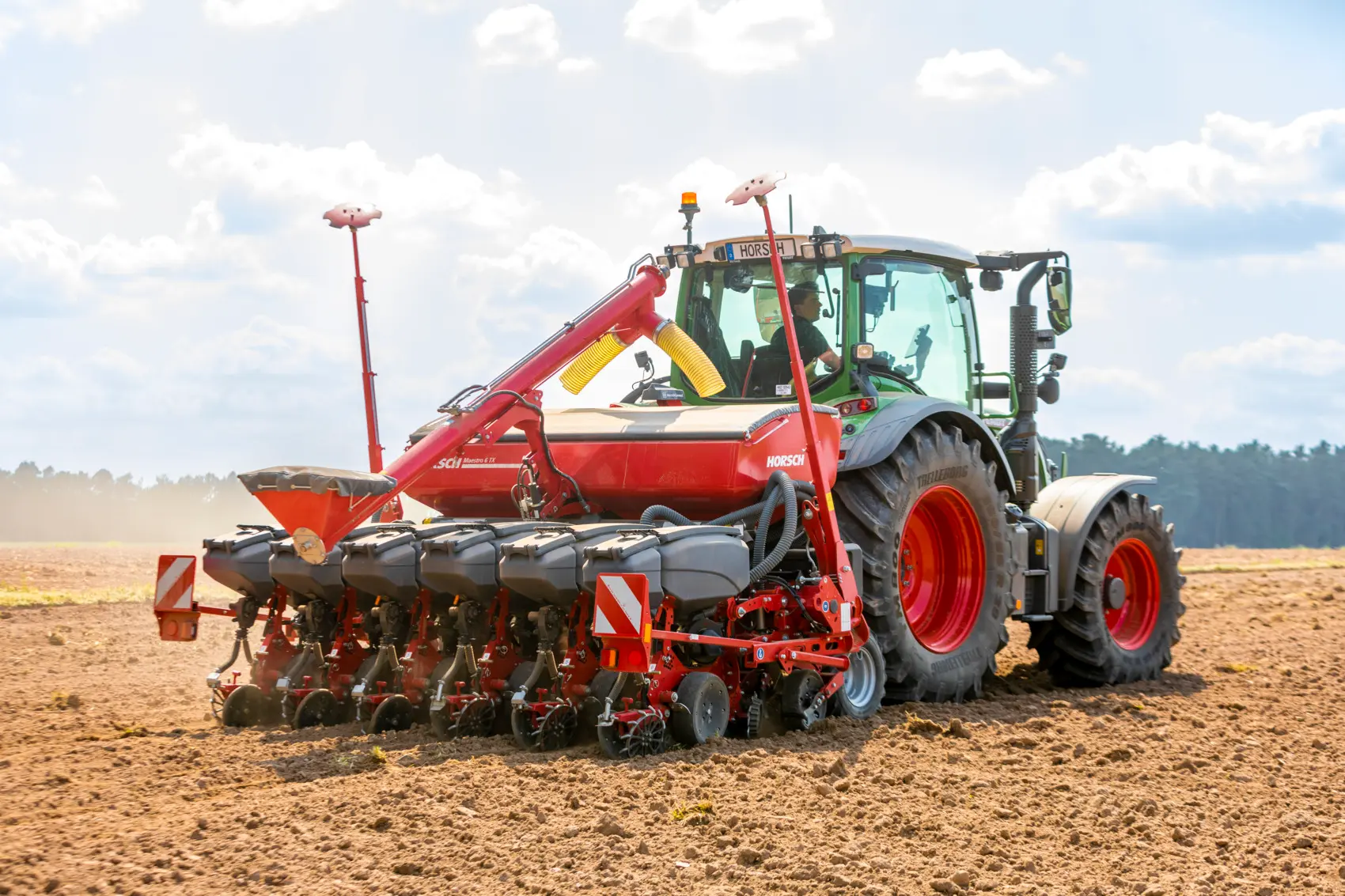 Zielony traktor Fendt ciągnący czerwony siewnik punktowy Horsch Maestro. Maszyna pracuje na suchym polu w słoneczny dzień, wzbijając za sobą widoczny kurz.